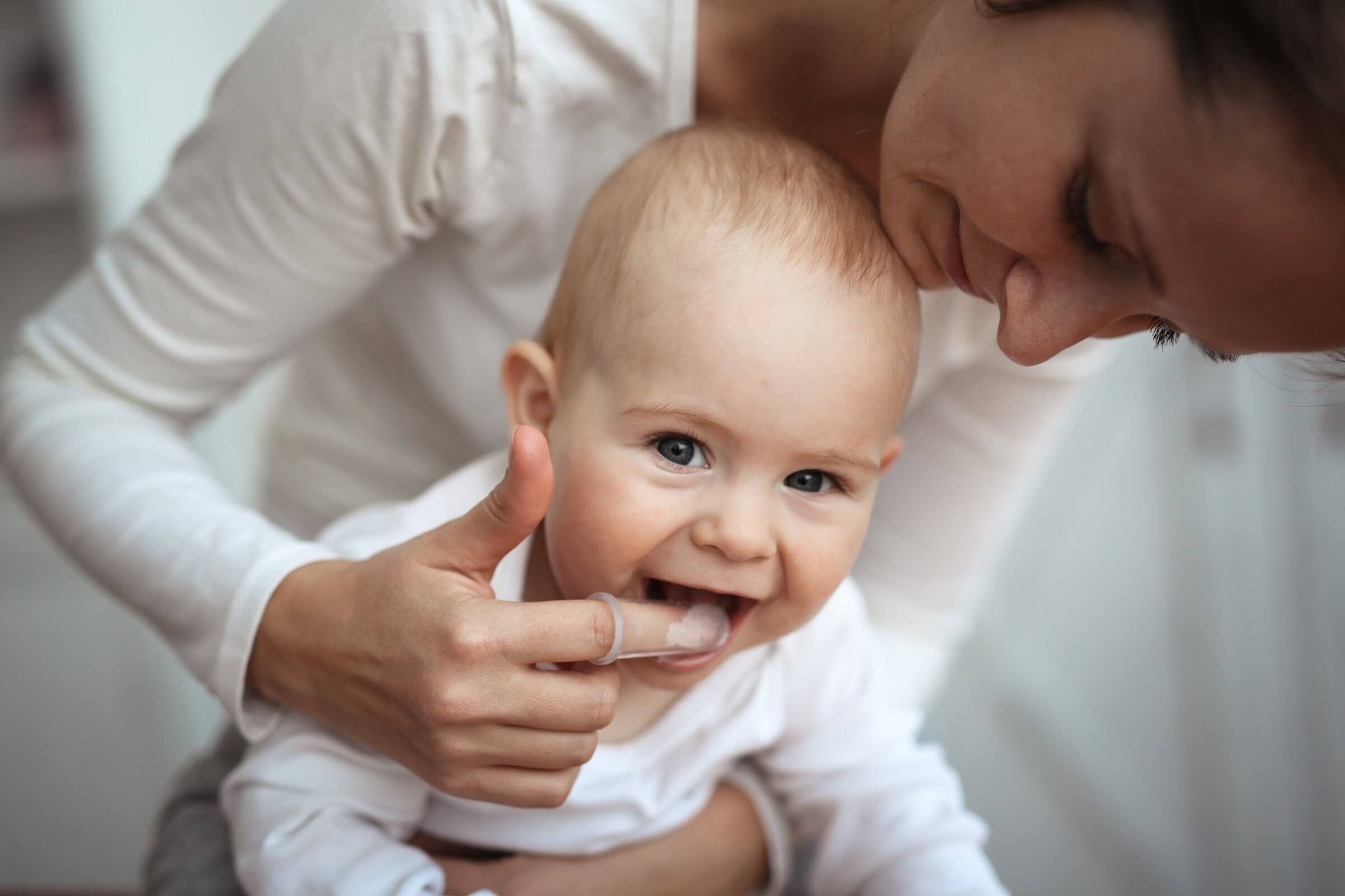 Mom cleaning her baby’s smile with a finger toothbrush.