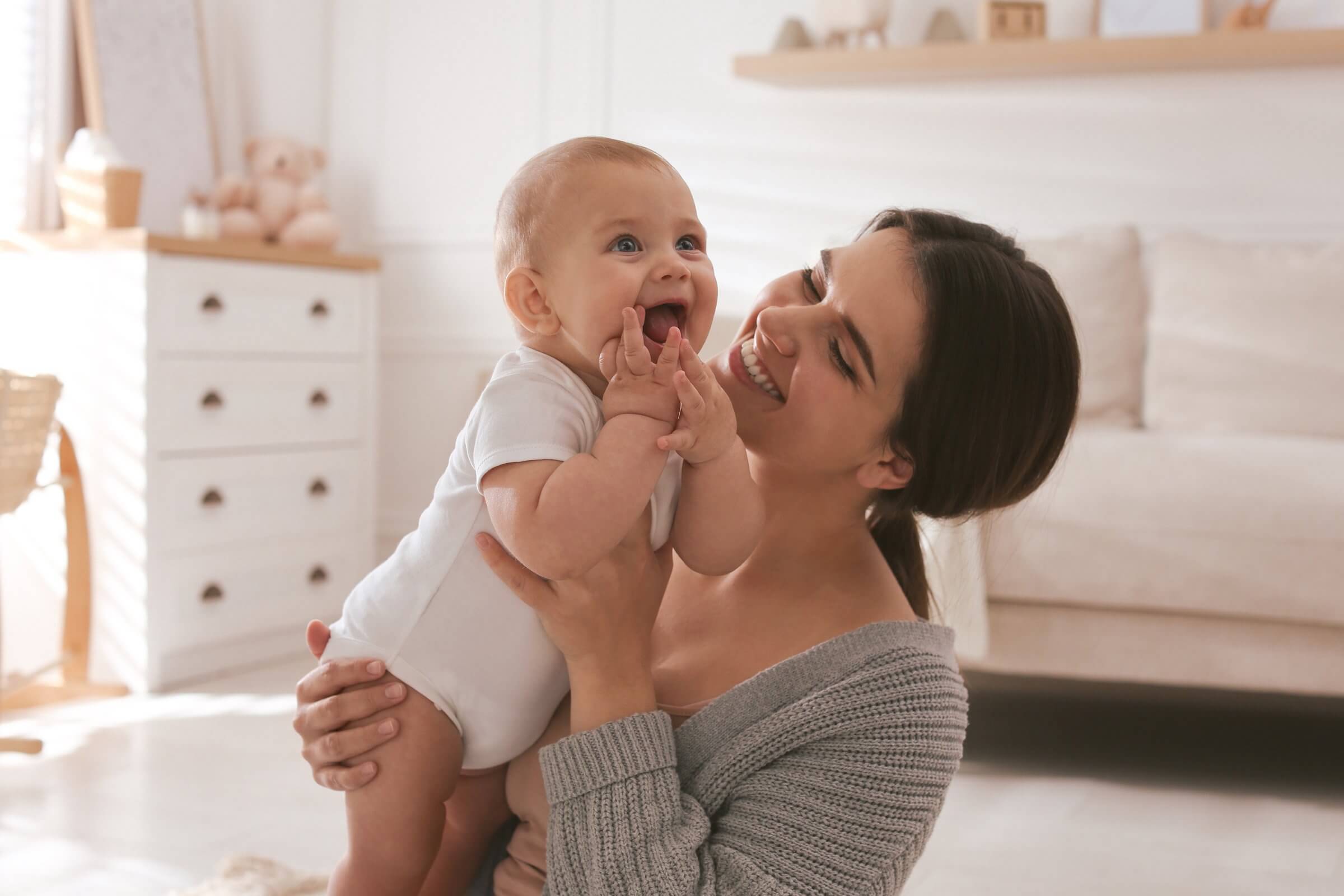 New mom smiling while holding her happy baby at home.