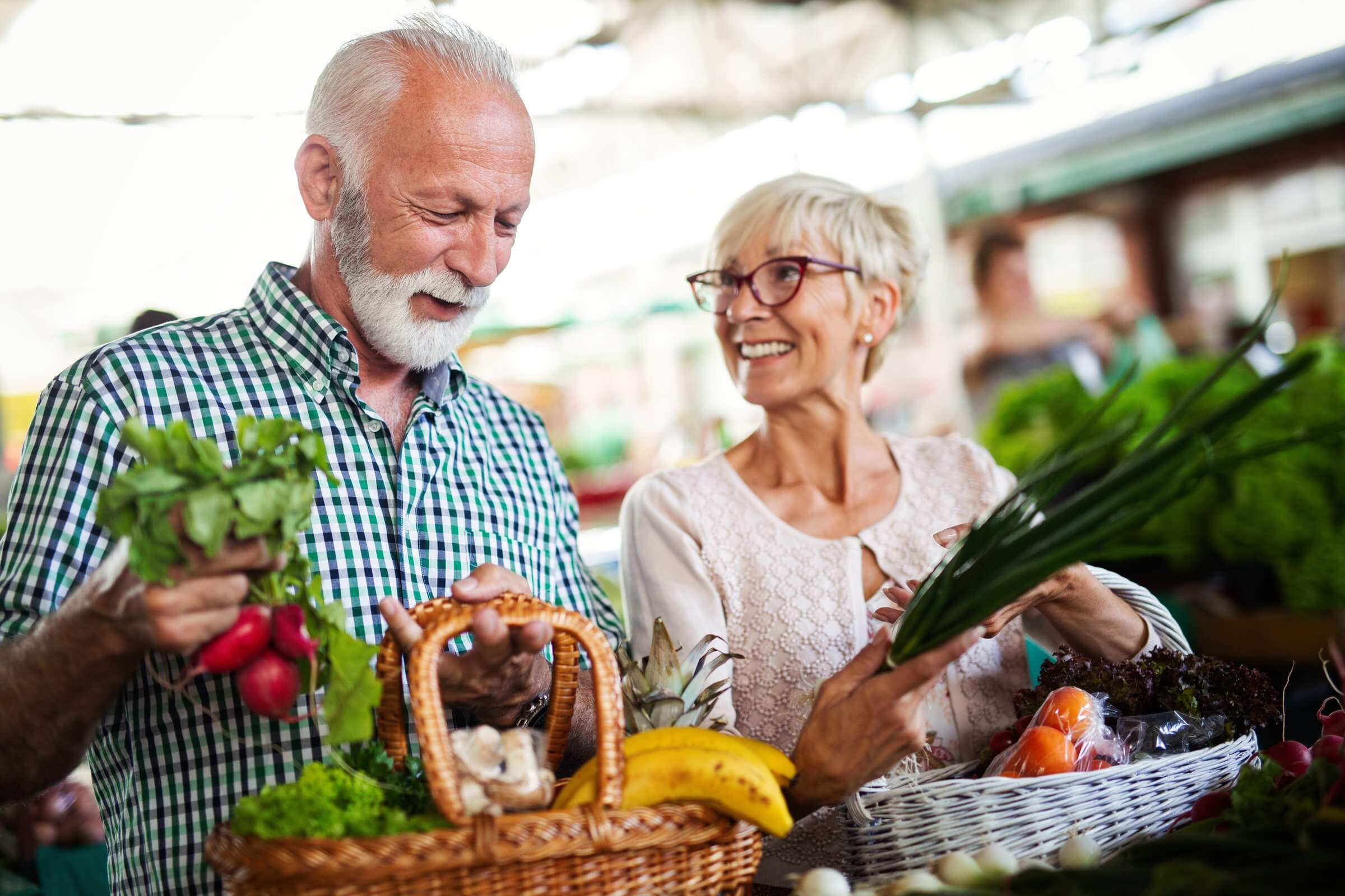 A senior couple smiling while they are shopping for tooth-healthy produce at a farmers' market
